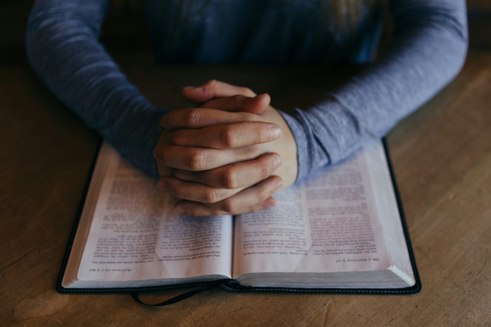 Hands folded in prayer over an open Bible